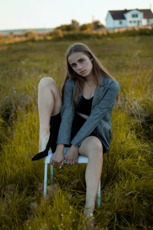 a woman sitting on a chair in a field, inspired by Elsa Bleda, unsplash, menacing pose, teenage girl, low quality photo, modeled