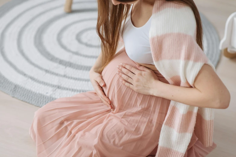 a pregnant woman is sitting on the floor, pexels contest winner, pink skirt, health supporter, neutral colours, covered with blanket