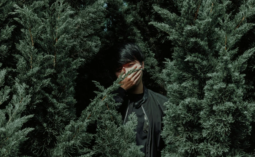 a man covering his face in front of some trees, an album cover, inspired by Elsa Bleda, pexels contest winner, surrealism, black and green, hong june hyung, hedge, male ulzzang