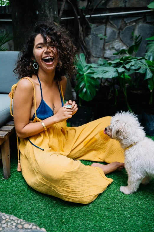 a woman sitting on the ground next to a white dog, pexels contest winner, happening, wavy hair yellow theme, mutahar laughing, justina blakeney, yellow overall