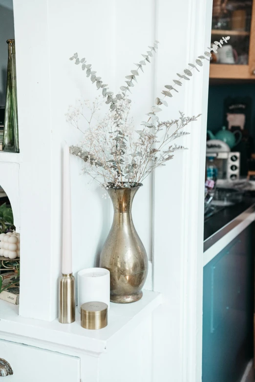 a vase filled with flowers sitting on top of a kitchen counter, by Sydney Carline, trending on unsplash, metallic brass accessories, shelves, dried fern, small hipster coffee shop