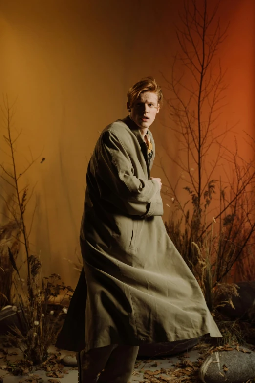 a man in a trench coat posing for a picture, an album cover, inspired by Nikolaj Abraham Abildgaard, renaissance, sophia lillis, forest style studio shot, fully covered in drapes, low iso