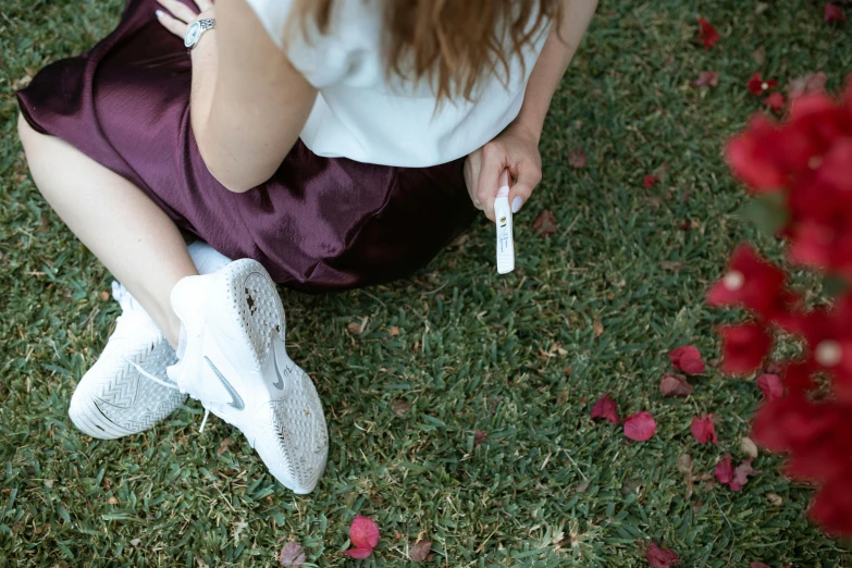 a woman sitting on the ground with a remote in her hand, trending on pexels, gum tissue, maroon and white, lawn, white petal