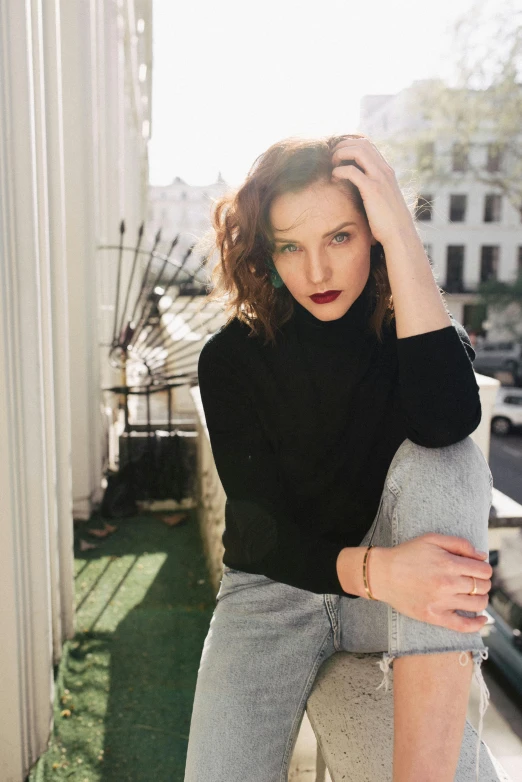 a woman sitting on a ledge in front of a building, inspired by Nan Goldin, trending on unsplash, renaissance, eleanor tomlinson, wearing a black sweater, laetitia casta, lipstick