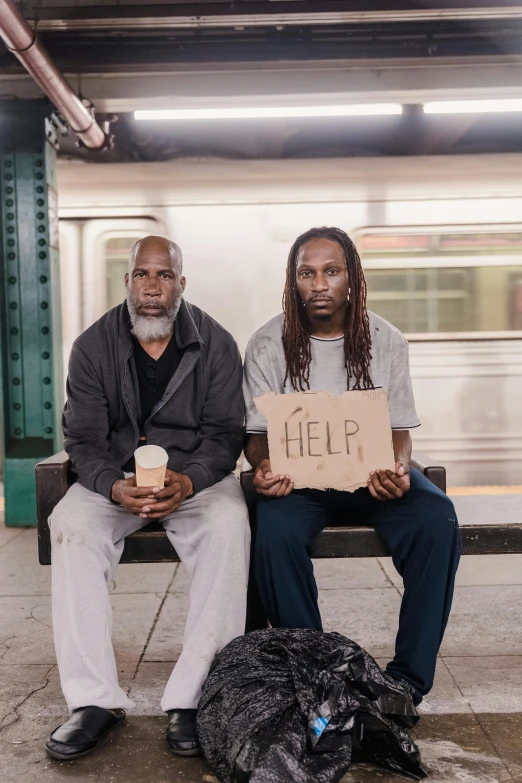 two men sitting on a bench holding signs, by Alison Geissler, trending on unsplash, renaissance, harlem, donald trump as a homeless man, train station, ( ( theatrical ) )