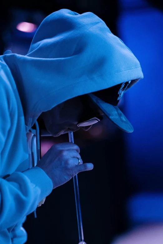 a man in a blue hoodie holding a microphone, by artist, trending on reddit, hood and shadows covering face, wearing white silk hood, close-up!!!!!!, performance