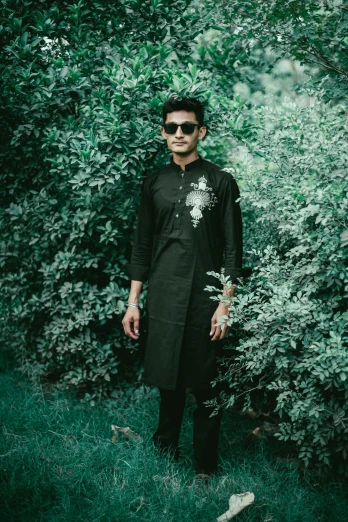 a man standing in the middle of a lush green forest, an album cover, by Riza Abbasi, pexels contest winner, wearing a kurta, black on black, dark shades, embroidered shirt