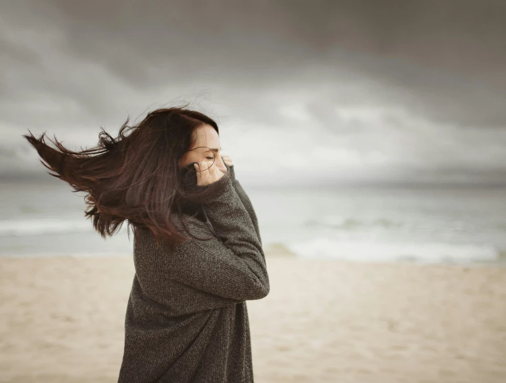 a woman standing on top of a sandy beach, an album cover, pexels contest winner, romanticism, windy hair, winter storm, stressed expression, grey