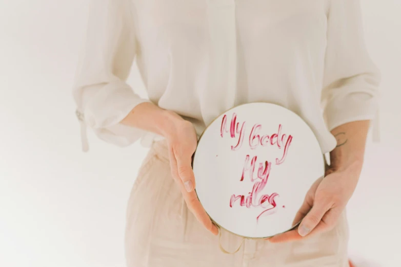 a woman holding a plate with writing on it, by Emma Andijewska, trending on pexels, velvet art, hey buddy, white background, fertility