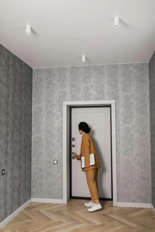 a woman standing in a room next to a door, wallpaper pattern, grey clothes, ignant, ƒ/2.5