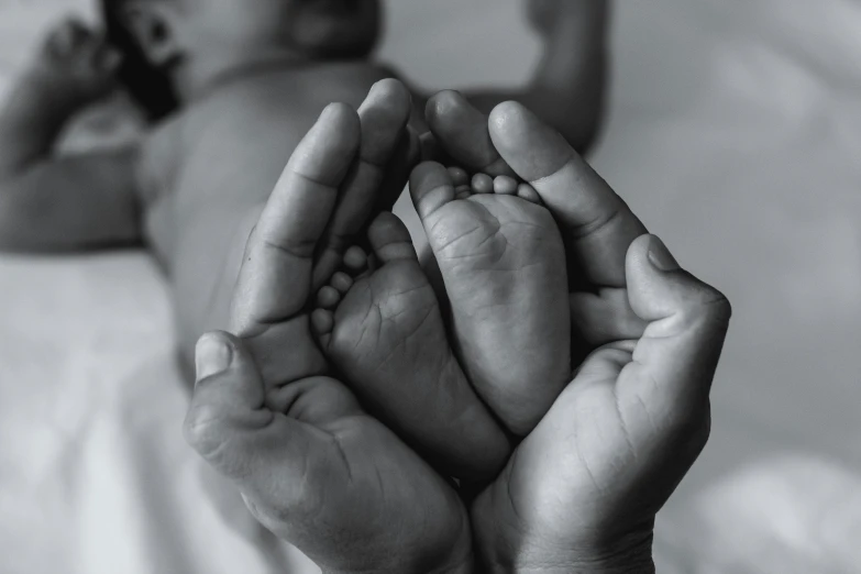 a black and white photo of a person holding a baby's foot, symbolism, healthcare, no watermarks, multiple limbs, color photo