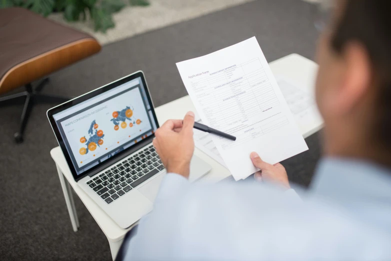 a man sitting at a table with a laptop and papers, a cartoon, unsplash, biotech, low quality photo, background image, loosely cropped