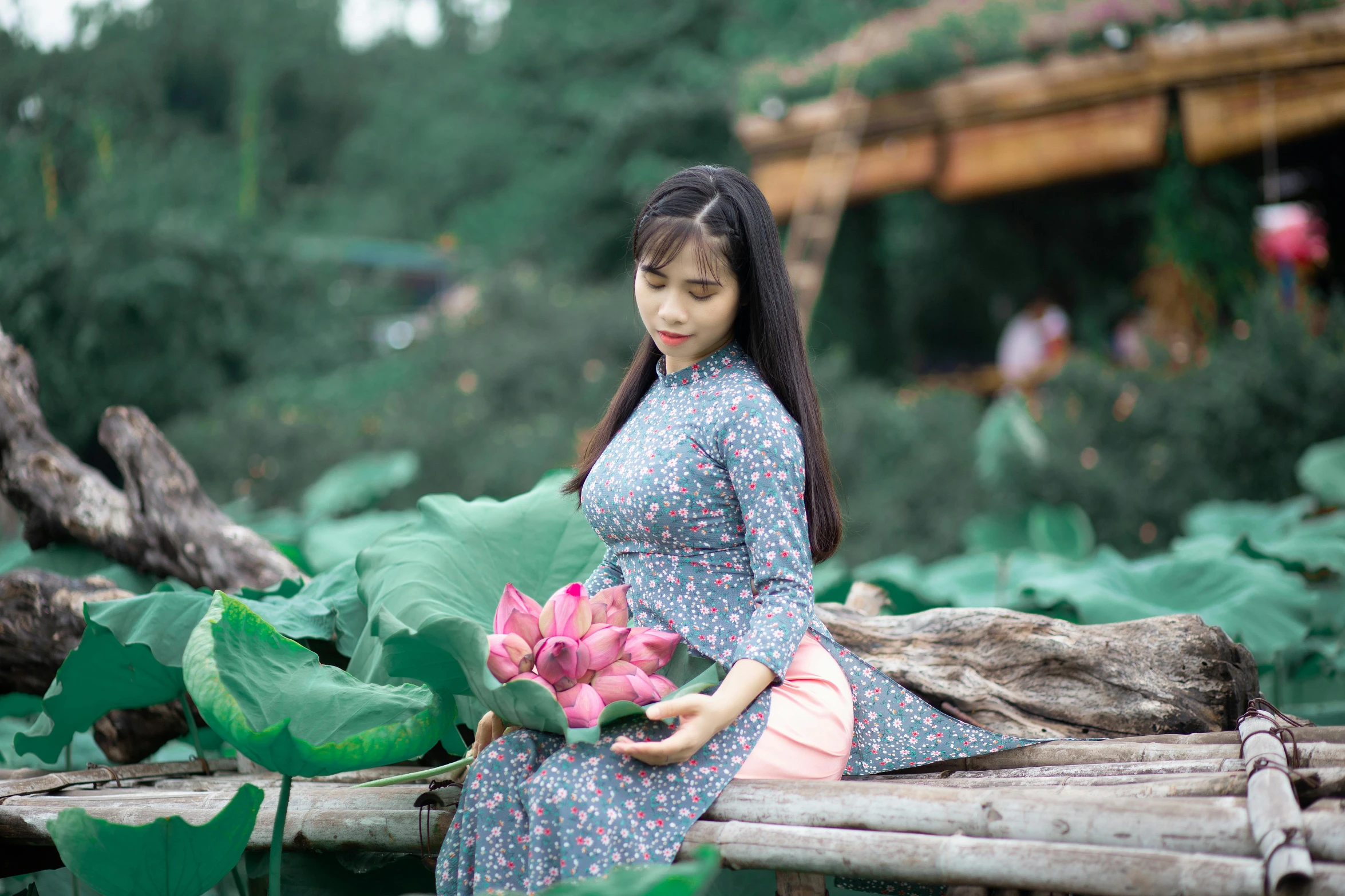 a woman sitting on a log holding a pink flower, inspired by Ruth Jên, pexels contest winner, ao dai, avatar image, traditional costume, standing on a lotus