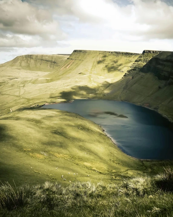 a large body of water sitting on top of a lush green hillside, by Hallsteinn Sigurðsson, pexels contest winner, les nabis, barren earth, wales, mountain lake, photo for a magazine