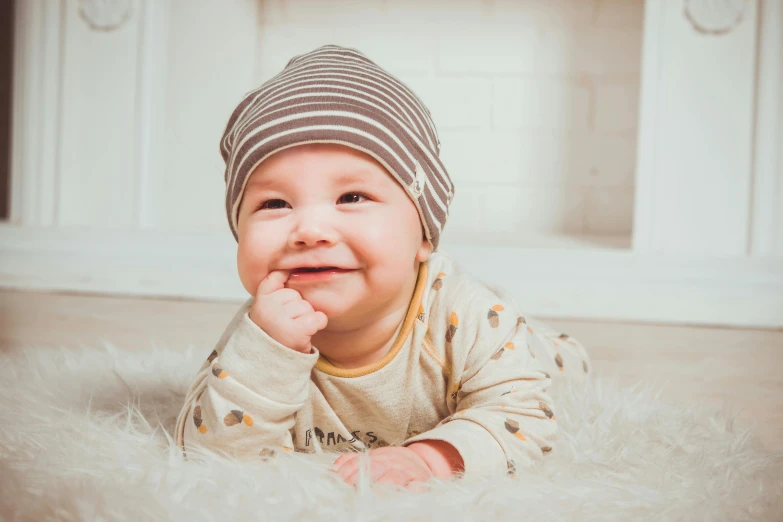 a baby laying on the floor wearing a hat, pexels contest winner, smiling male, beanie, 1 4 9 3, portrait image