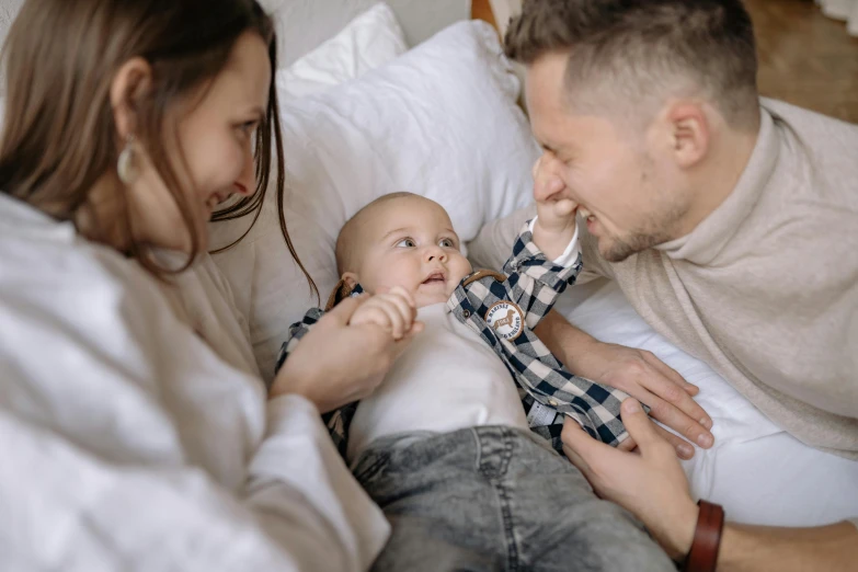 a man sitting on top of a bed next to a woman holding a baby, pexels contest winner, incoherents, white cheeks, 1 2 9 7, small ears, thumbnail