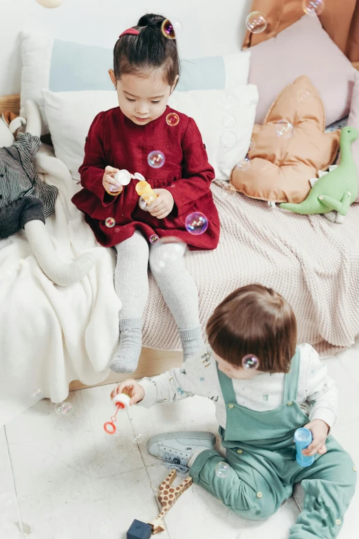 two little girls sitting on a bed playing with toys, inspired by Elsa Beskow, instagram, children playing with pogs, red and blue garments, customers, mini planets