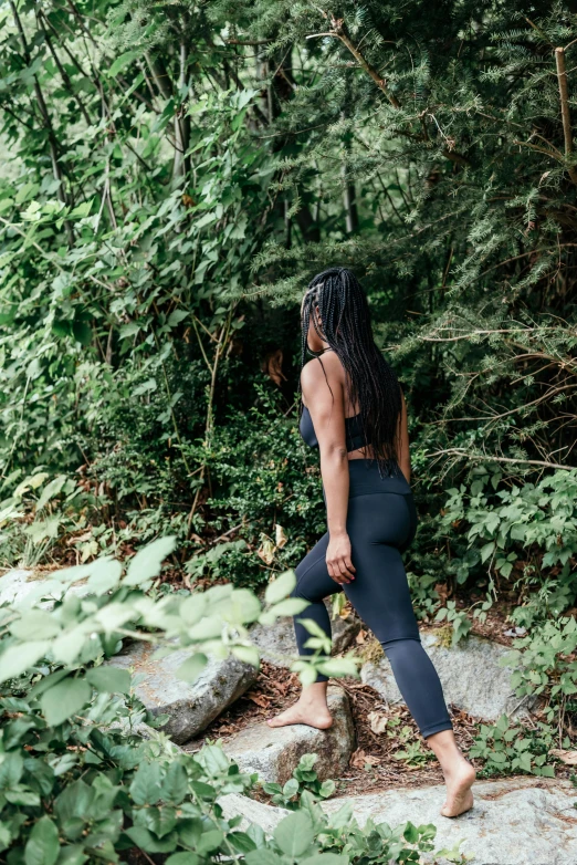 a woman walking down a path in the woods, by Dulah Marie Evans, wearing a cropped black tank top, climbing up a cliffside, leggings, jamaica