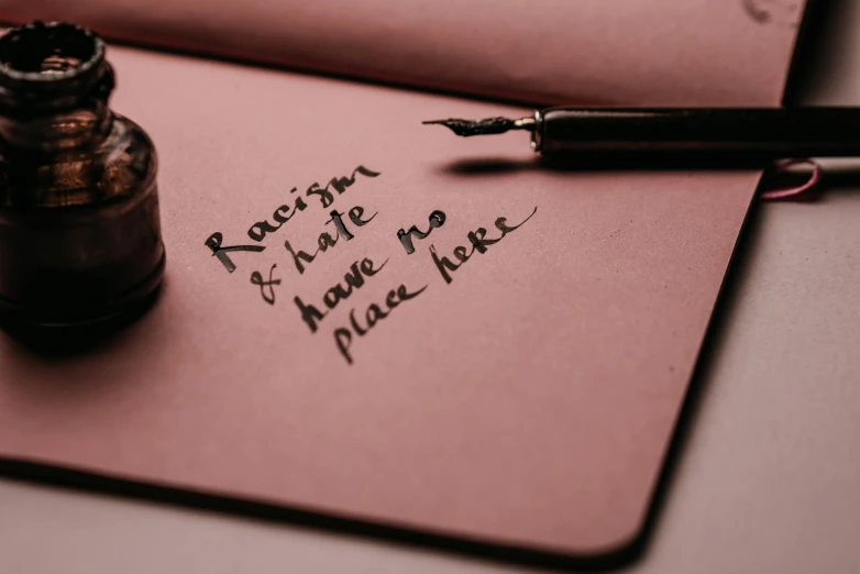 a fountain pen sitting on top of a piece of paper, an album cover, by Arabella Rankin, pexels, letterism, pink and black, any racial background, hate, background image