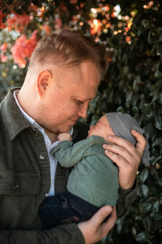 a man holding a baby in his arms, by Winona Nelson, unsplash, edmund blair and charlie bowater, in the garden, lgbtq, caring fatherly wide forehead