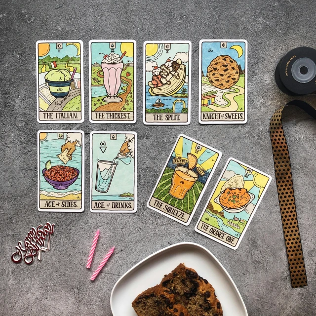 a table topped with a plate of cake and tarot cards, flatlay, reverse, detailed product image, the best