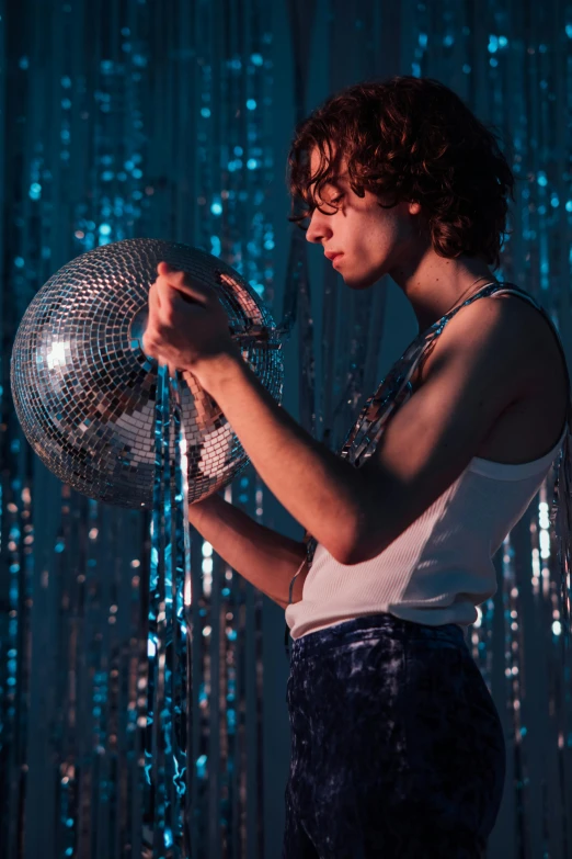 a woman standing in front of a disco ball, an album cover, inspired by Nan Goldin, trending on pexels, magical realism, thin young male, robert sheehan, holding maracas, sophia lillis