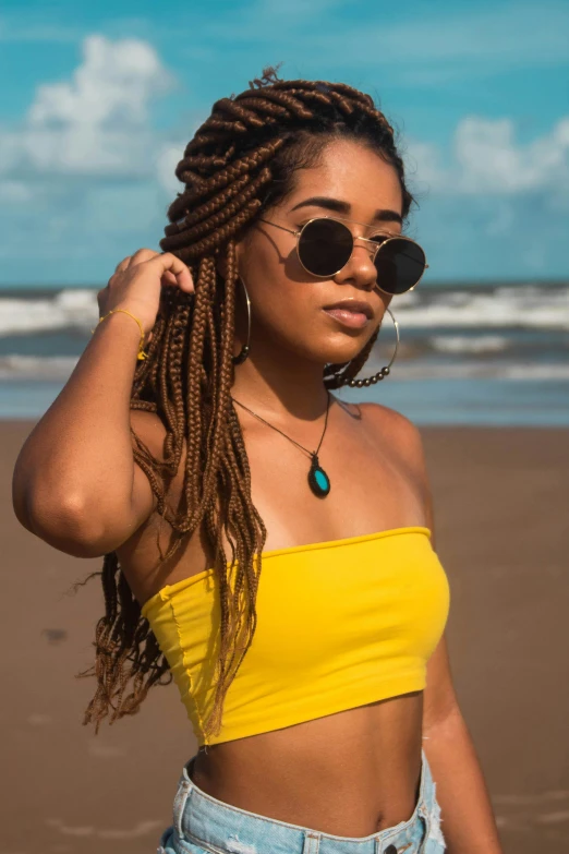 a woman standing on top of a beach next to the ocean, trending on pexels, wavy hair yellow theme, cornrows, dark shades, avatar image