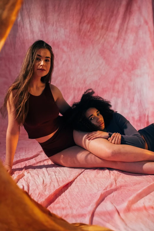 a couple of women laying on top of a bed, by Jessie Alexandra Dick, trending on pexels, renaissance, pink studio lighting, wearing a crop top, lorde, round thighs