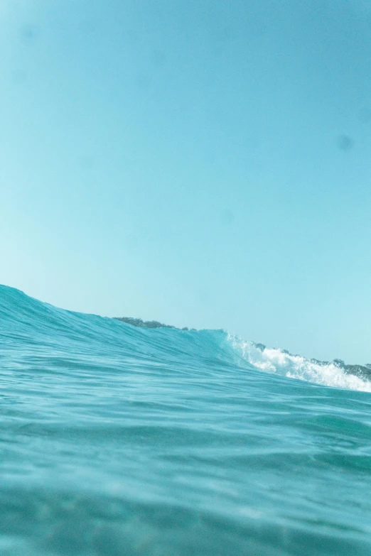 a man riding a wave on top of a surfboard, from afar, light blue water, low quality photo, teal