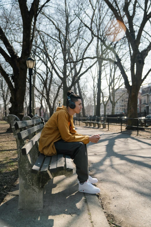 a man sitting on a bench in a park, an album cover, trending on unsplash, wearing a headset, in new york, ignant, ( ( theatrical ) )