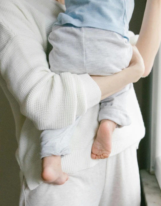 a woman holding a baby in her arms, incoherents, wearing white pajamas, light grey mist, wearing pants, zoomed in