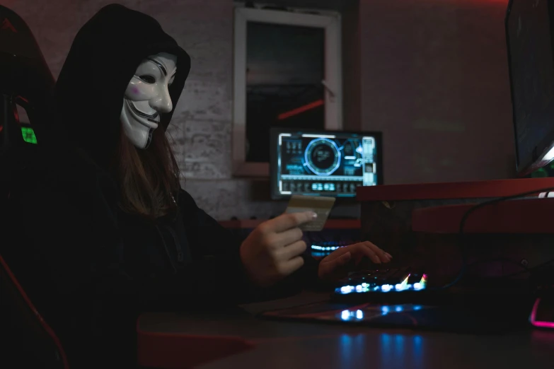 a person wearing a mask sitting in front of a computer, pexels contest winner, holography, female thief, a black cloak, jigsaw, ( ( theatrical ) )