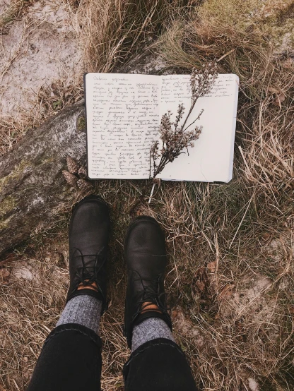 a person standing next to a book on the ground, a picture, by Lucia Peka, unsplash contest winner, nature journal, found scribbled in a notebook, goth aesthetic, 🤠 using a 🖥