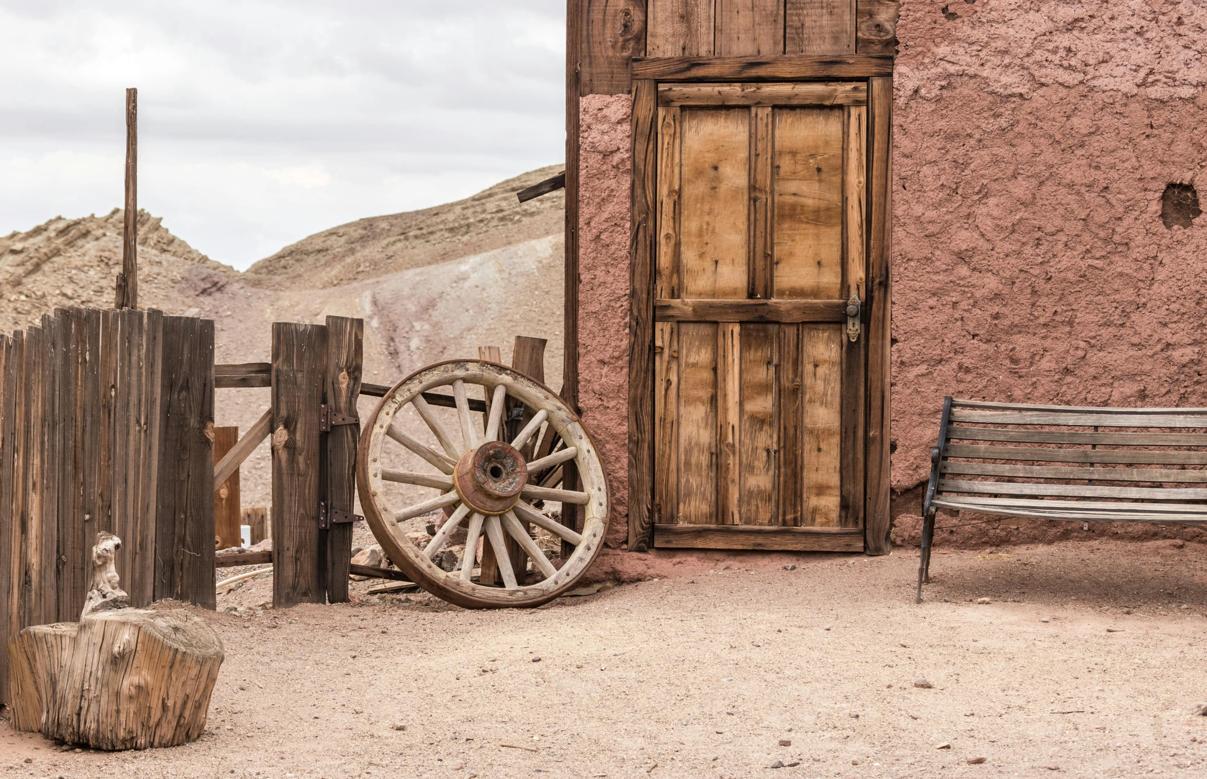 a wooden bench sitting in front of a building, by Linda Sutton, pexels contest winner, steampunk desert background, pink door, rock and dust, cart wheels