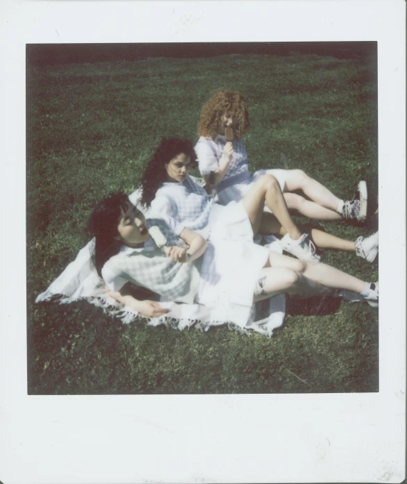 a group of women sitting on top of a lush green field, a polaroid photo, inspired by Nan Goldin, curly bangs, an all white human, charli xcx, three women