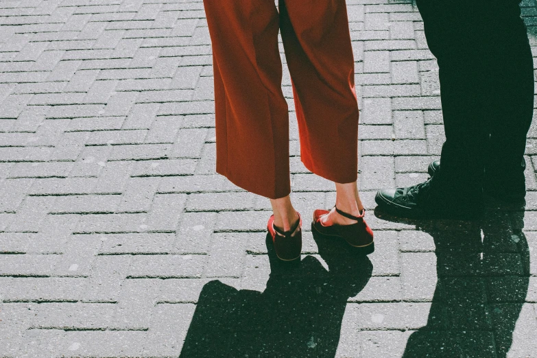 two people standing next to each other on a sidewalk, trending on pexels, antipodeans, red and black details, platforms, maroon red, summer light