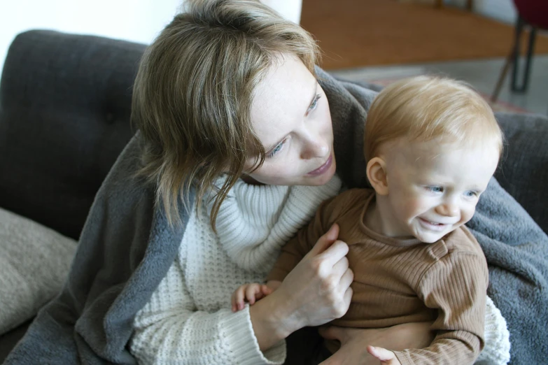 a woman sitting on a couch holding a baby, pexels, hurufiyya, warm coloured, casually dressed, thumbnail, pale-skinned