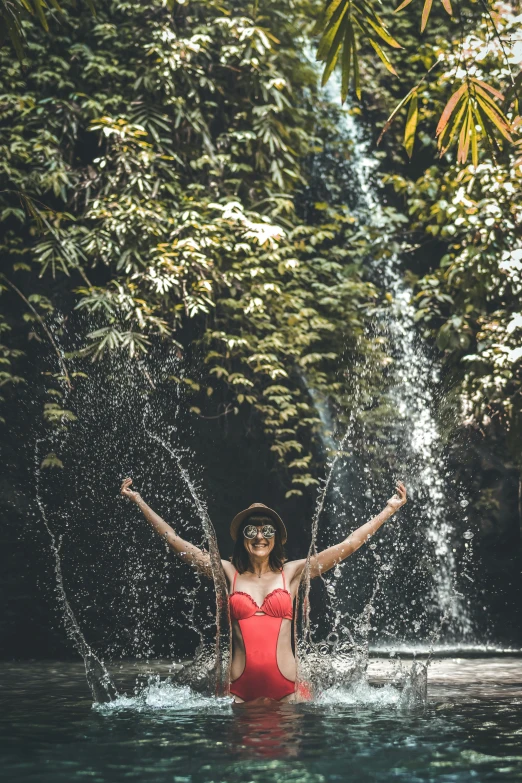 a woman in a red swimsuit in front of a waterfall, by Cherryl Fountain, pexels contest winner, with arms up, tropics, covered in vines, full frame image