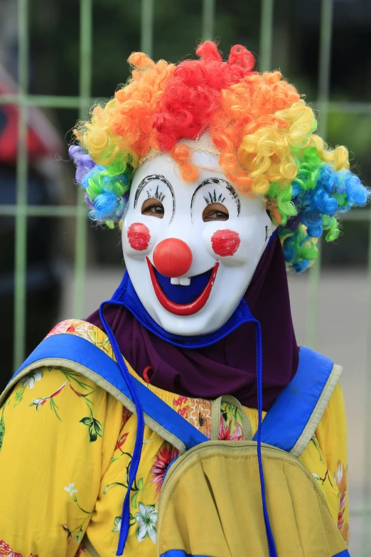 a clown is standing in front of a fence, smiling for the camera, full of colours, square, zoomed in