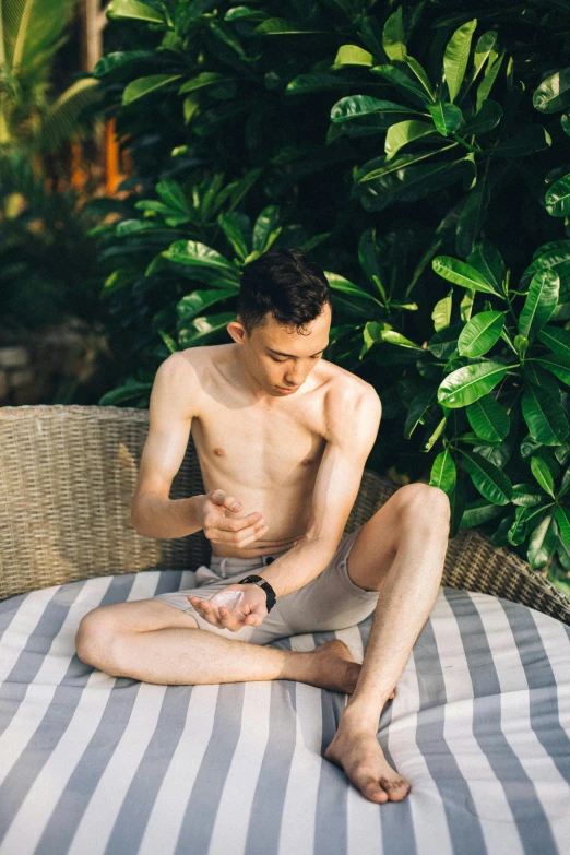 a man sitting on top of a bed next to a bush, inspired by Ren Hang, unsplash, palm skin, partially cupping her hands, poolside, thin young male