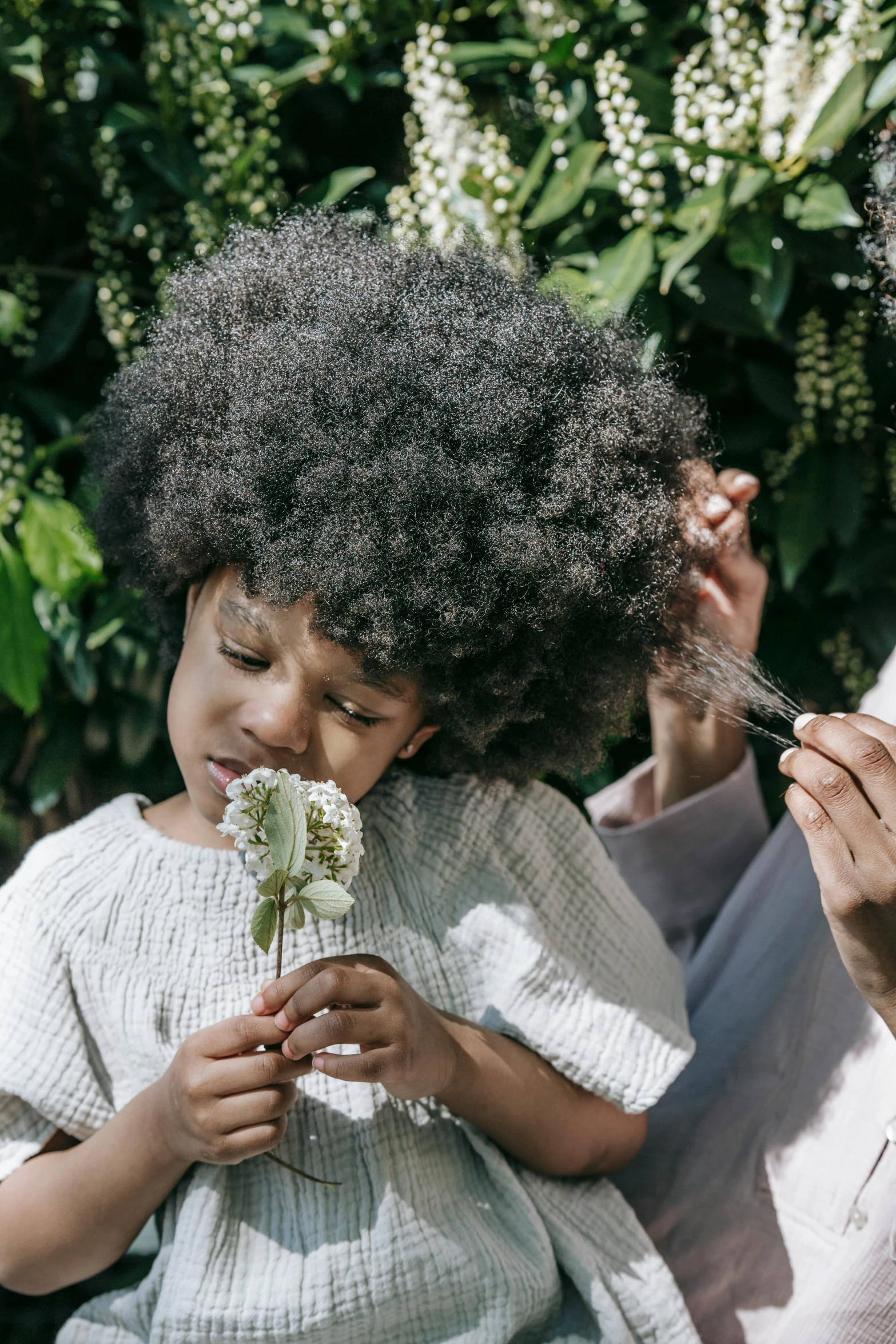 a woman sitting next to a little girl holding a flower, an album cover, pexels contest winner, natural hair, lush greens, afro tech, salt and pepper hair