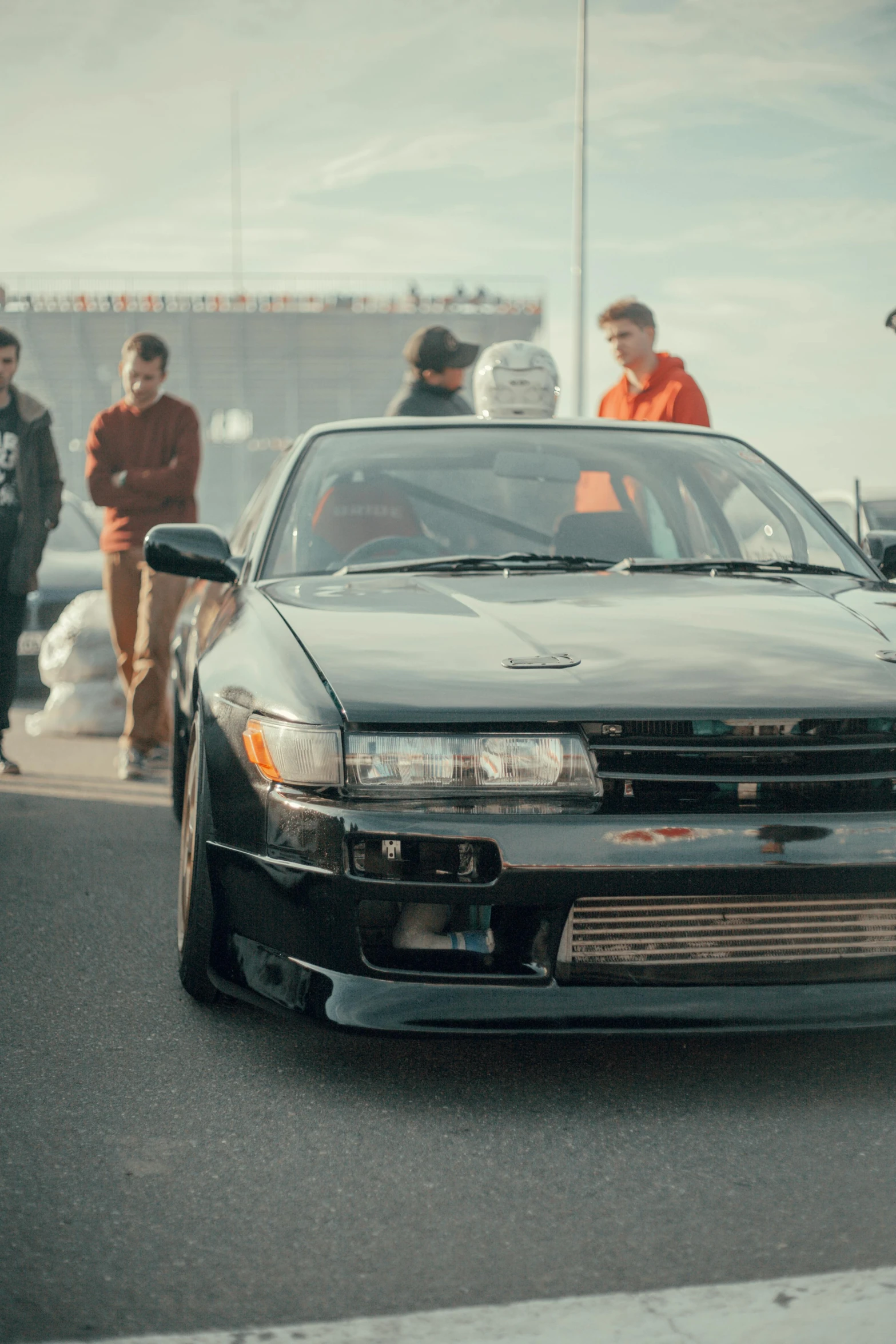 a group of people standing around a car, on a street race track, intense look, drifting around a corner, avatar image