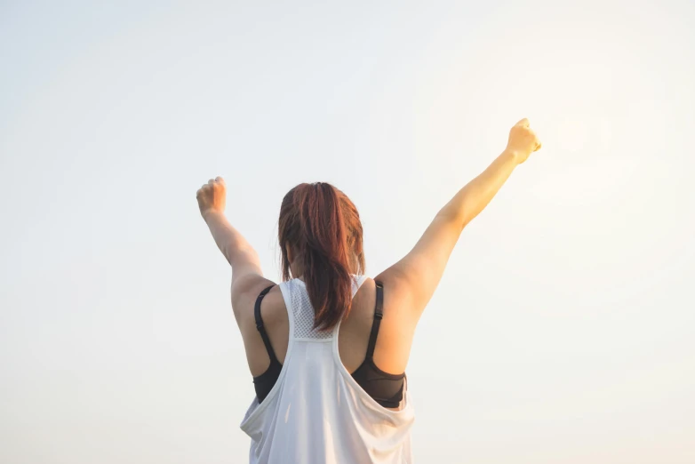 a woman raising her arms in the air, pexels contest winner, wearing a muscle tee shirt, victory lap, full daylight, hunched shoulders