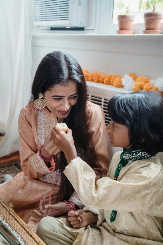 a woman sitting next to a little girl in front of a mirror, wearing a silk kurta, celebrating, promotional image, square