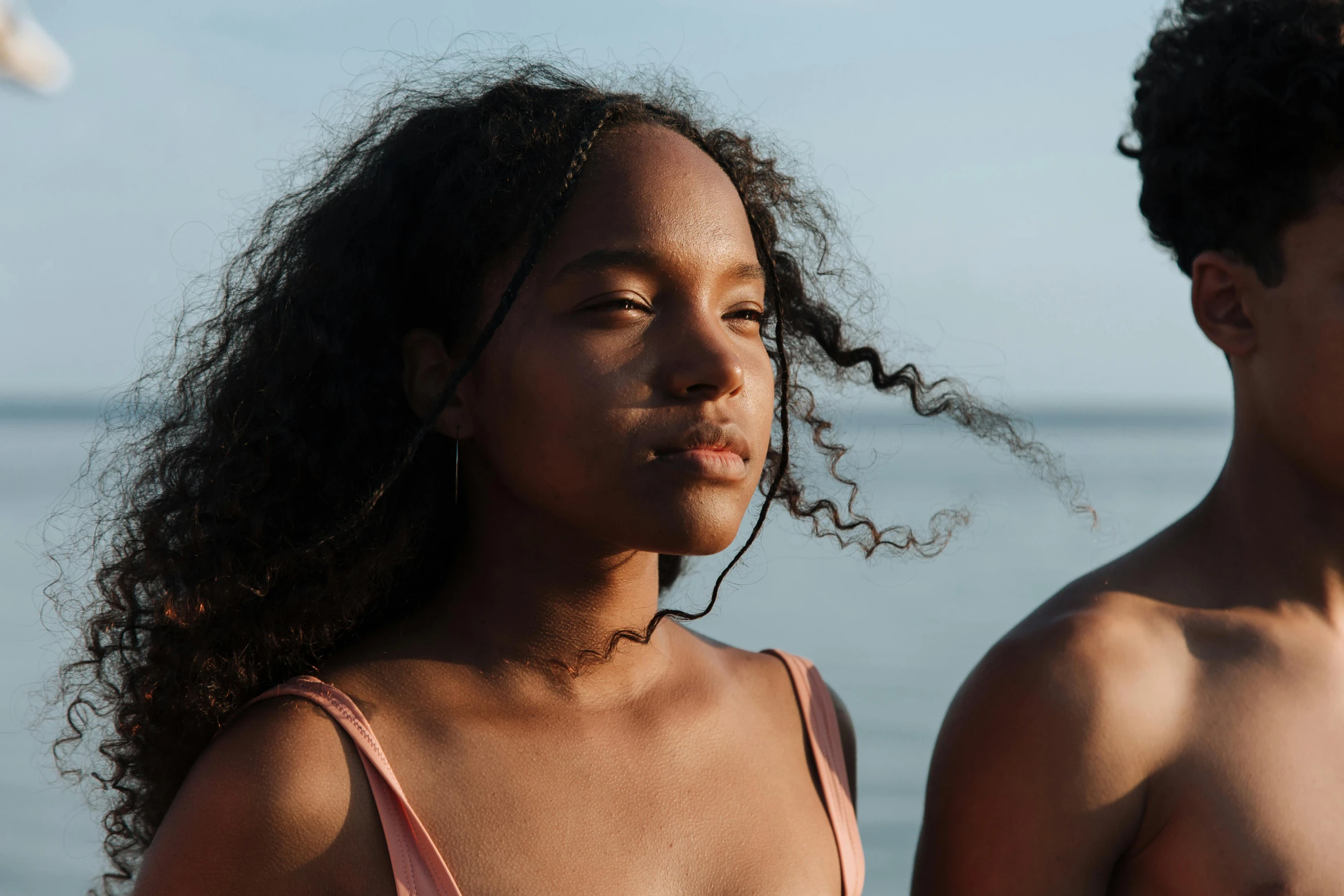 a couple of young people standing next to each other, by Carey Morris, trending on pexels, happening, sunbathed skin, black teenage girl, looking serious, wavy hair spread out