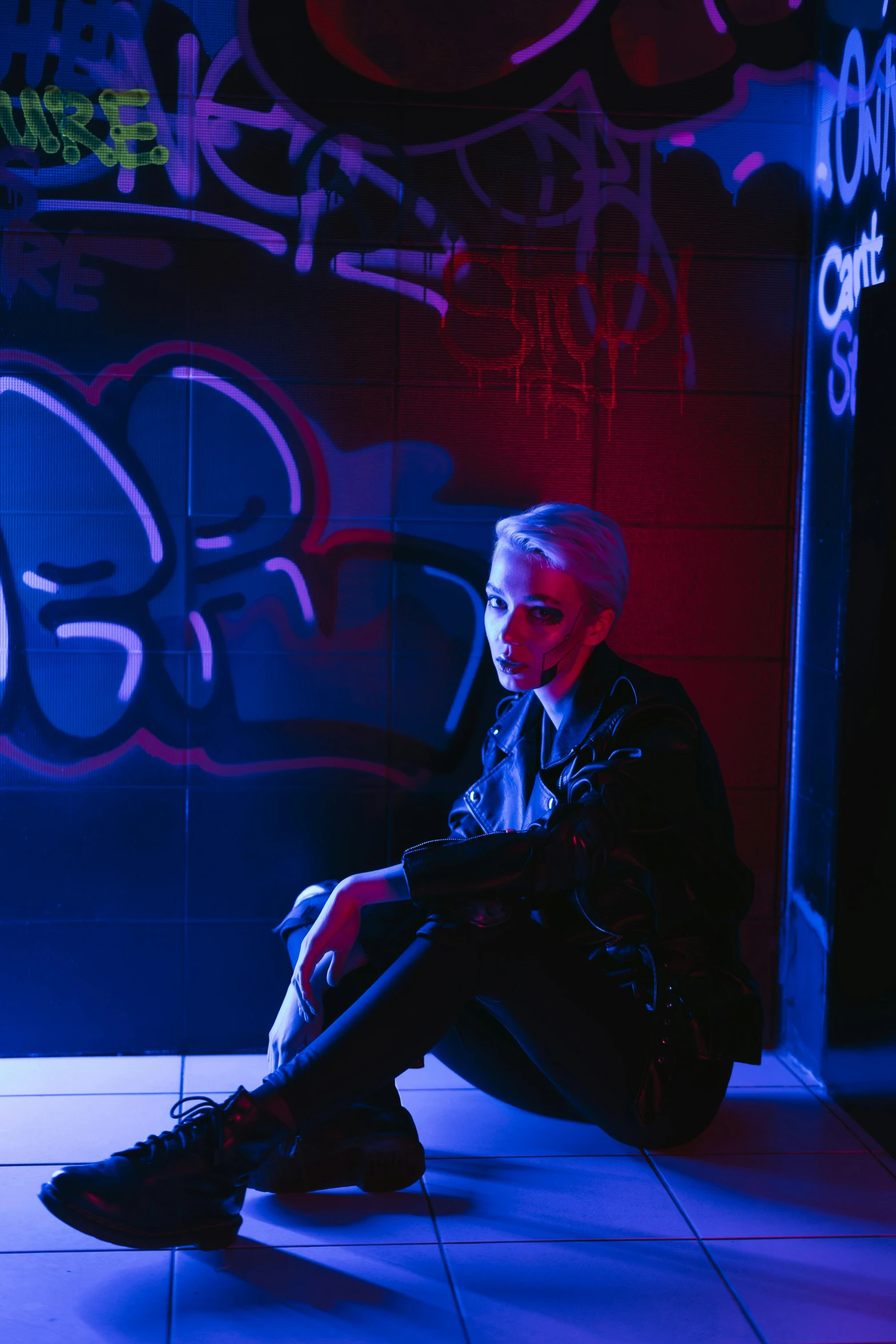 a man sitting on the ground in front of a graffiti covered wall, an album cover, inspired by Elsa Bleda, trending on pexels, short platinum hair tomboy, purple scene lighting, ariana grande as a sith, in a black room