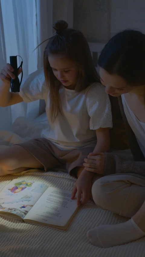 a woman and a little girl sitting on a bed reading a book, a cartoon, by Adam Marczyński, pexels contest winner, flashlight on, integrating with technology, still from a live action movie, high angle shot