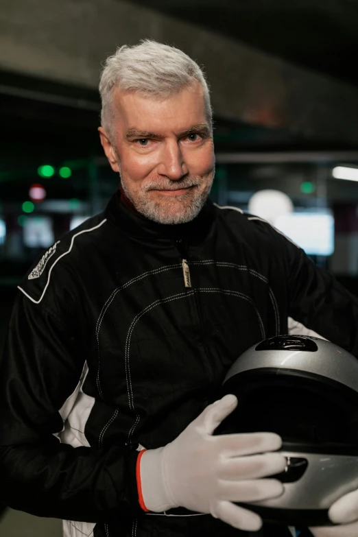 a man holding a helmet in a parking garage, inspired by Graham Forsythe, white hair and white beard, on a street race track, flight suit and gloves, with a black background