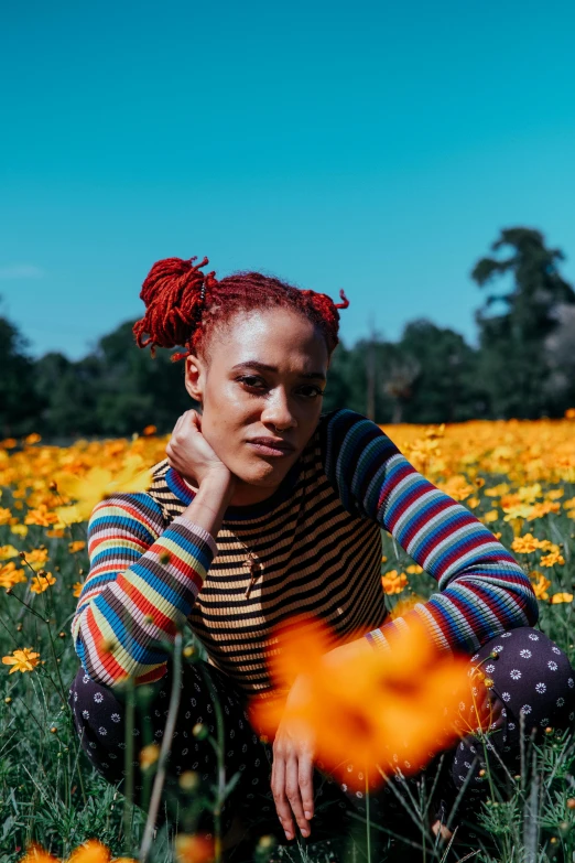 a woman sitting in a field of flowers, inspired by Jessie Alexandra Dick, trending on pexels, color field, red afro, casually dressed, sydney park, orange braided hair