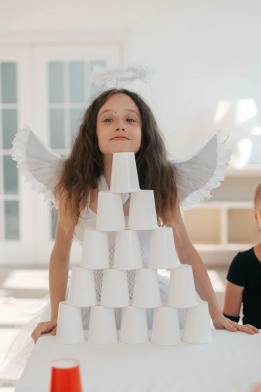a little girl sitting on top of a table next to a little boy, by Marie Angel, pexels contest winner, interactive art, paper cup, epic angel wings, bulky build, two organic looking towers